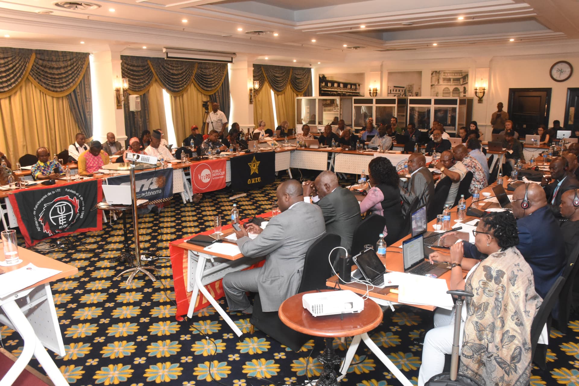 Delegates seated around a large U-shaped table with union banners — PSI, O.W.T.U., and others